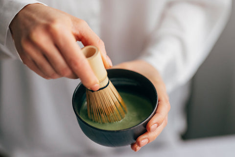 A cup of ceremonial grade matcha being whisked with a chasen
